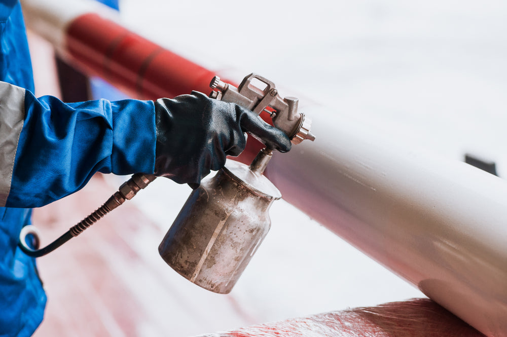 Spraying paint by hand onto a metal pipe