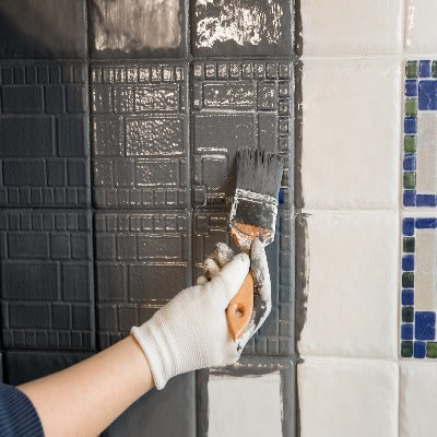 Hand painting white ceramic tiles with grey paint and a paint brush