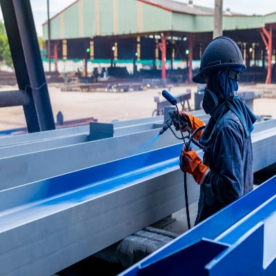 Person spraying blue paint onto steel beam